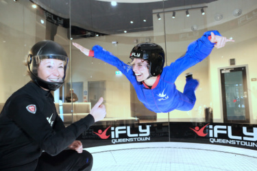 Instructor smiles and gives 'thumbs up' as another smiling woman floats in the wind tunnel
